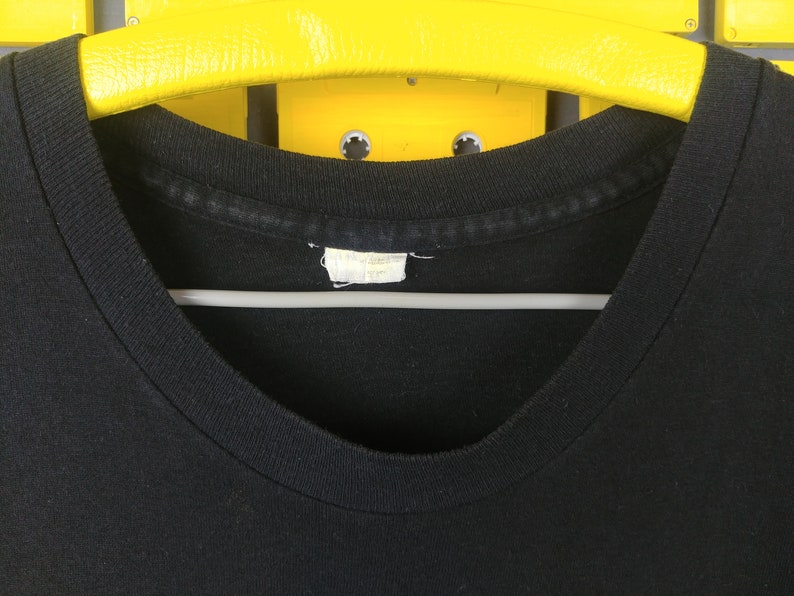 May include: Close-up of the neck of a black t-shirt with a white tag. The tag is blank.