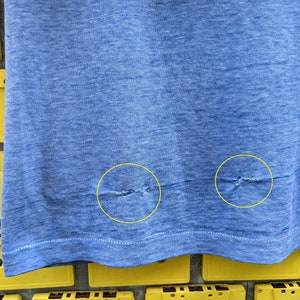 Puede incluir: Primer plano de una camiseta azul con dos peque&ntilde;os agujeros cerca del dobladillo inferior.