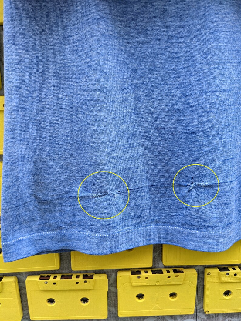 Puede incluir: Primer plano de una camiseta azul con dos peque&ntilde;os agujeros cerca del dobladillo inferior.