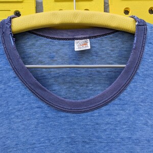 Puede incluir: Una camiseta azul con un cuello de canal&eacute; azul oscuro y una etiqueta de Hanes. La camiseta est&aacute; hecha de una tela suave y ligera.