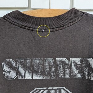 May include: Close-up of a dark gray t-shirt with the word "SHEARER" printed in a distressed, white font. The shirt's collar is ribbed and dark gray. The shirt appears to be made of a soft material.