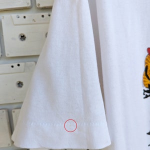 May include: White t-shirt with a small, light brown stain on the bottom of the sleeve.