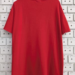 May include: A plain red t-shirt with short sleeves. The shirt is hanging on a wooden hanger against a white background.