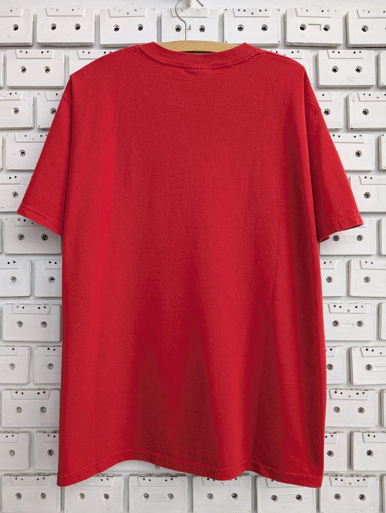 May include: A plain red t-shirt with short sleeves. The shirt is hanging on a wooden hanger against a white background.