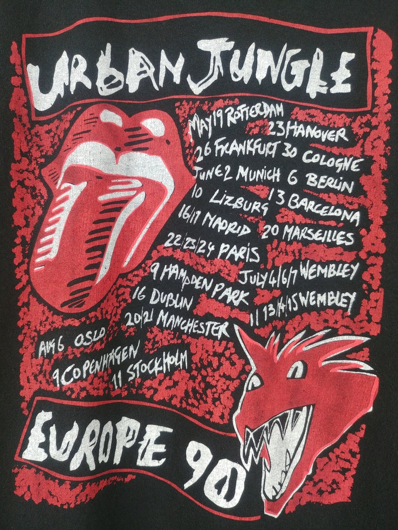 May include: Black t-shirt with a red and white graphic of a tongue and a dragon. The text "URBAN JUNGLE" is at the top of the graphic and "EUROPE 90" is at the bottom. The graphic also includes a list of cities and dates for a tour.