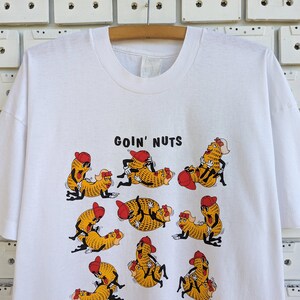 May include: White t-shirt with a graphic of peanuts in various poses with the text "Goin' Nuts" printed on the front.