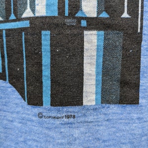 Puede incluir: Una camiseta azul con un dise&ntilde;o geom&eacute;trico en blanco y negro. La camiseta tiene el texto "COPYRIGHT 1978" impreso en la parte inferior.