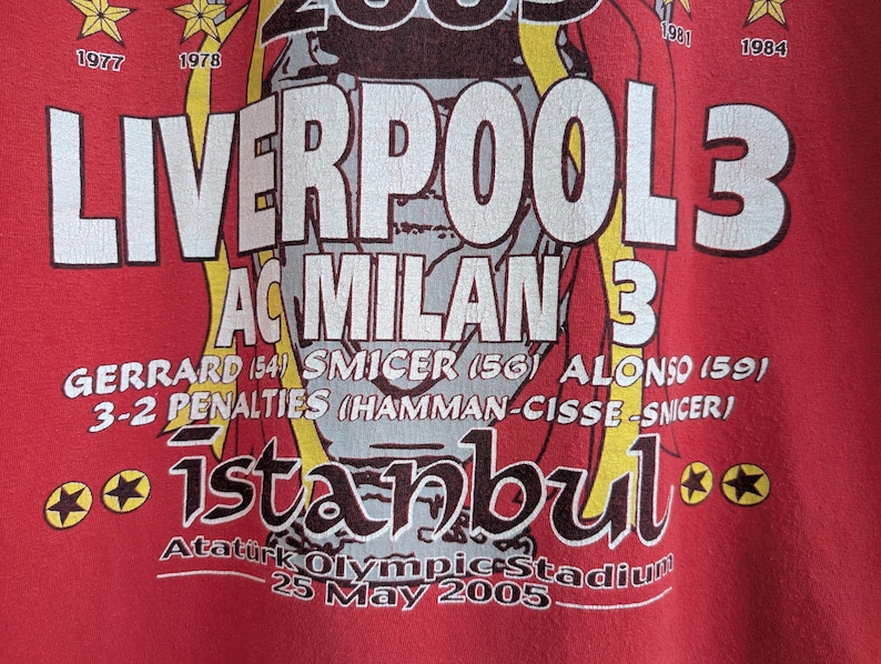 May include: Red t-shirt featuring the text "LIVERPOOL 3 AC MILAN 3" with player names and the word "istanbul". The shirt also includes the date "25 May 2005" and star graphics.