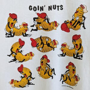 May include: A white t-shirt with a graphic of peanuts in various poses with the text "Goin' Nuts".