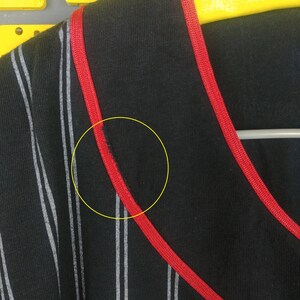 May include: Black and white striped shirt with red trim around the neckline. The shirt has a small tear near the neckline.