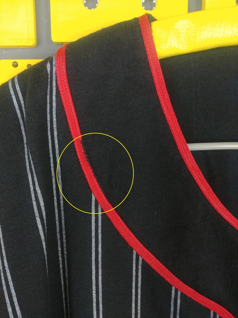 May include: Black and white striped shirt with red trim around the neckline. The shirt has a small tear near the neckline.