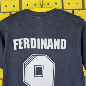 May include: Black t-shirt with white text that reads "FERDINAND" and a white number "9" on the back.