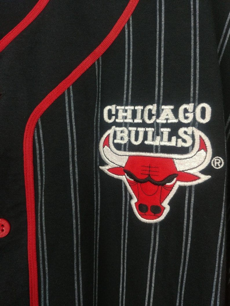 May include: Black and white striped baseball jersey with a red embroidered Chicago Bulls logo featuring a red bull with white horns and a registered trademark symbol.