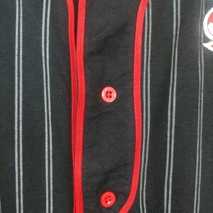 May include: Black and white striped baseball jersey with red trim and red buttons. The jersey has a small logo on the right side.