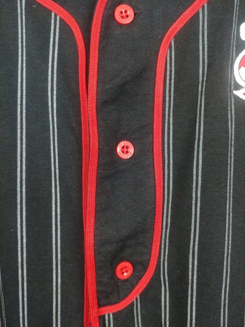 May include: Black and white striped baseball jersey with red trim and red buttons. The jersey has a small logo on the right side.