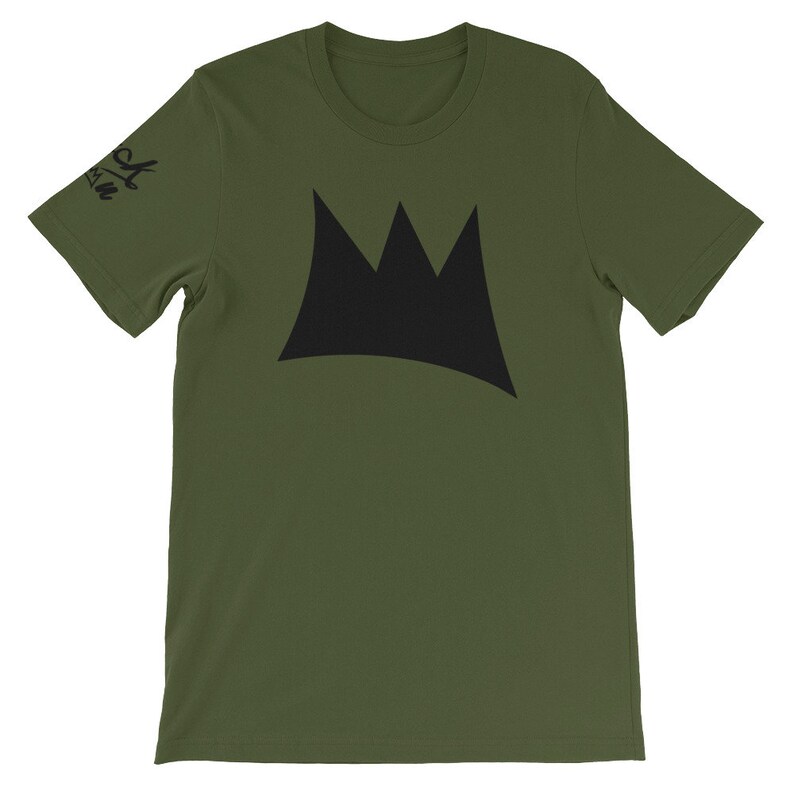 May include: Olive green t-shirt featuring a large black crown design on the front. The short-sleeved shirt has a crew neck and a small black text on the left sleeve. The shirt is made of a soft material.