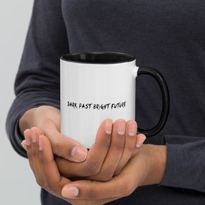 May include: White ceramic mug with a black interior and handle. The mug features the text "DARK PAST BRIGHT FUTURE" in black, handwritten-style lettering. The mug is held in both hands.