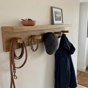 Hallway with soft white walls, solid oak shelf with 5 pegs and a top shelf. dog lead and dog collar hanging on the pegs along with a hat hook and coat hook. key holder on the shelf.