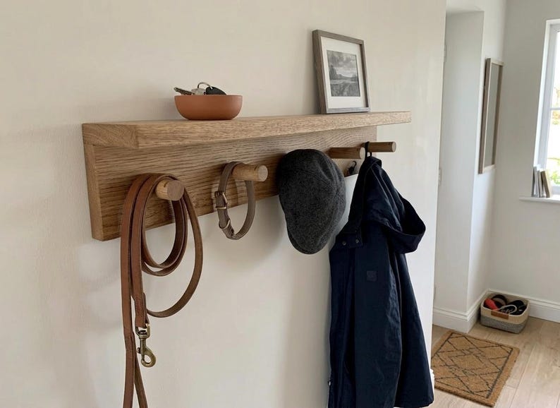 Hallway with soft white walls, solid oak shelf with 5 pegs and a top shelf. dog lead and dog collar hanging on the pegs along with a hat hook and coat hook. key holder on the shelf.
