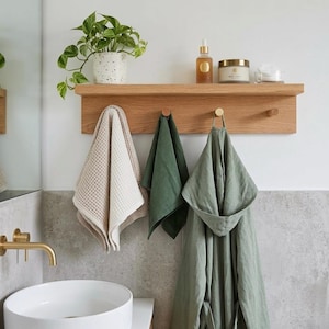 Bathroom towel holder in a modern bathroom with round sink and brass hardware. skin care on the shelf a trailing plant, and a robe hanging on a hook.