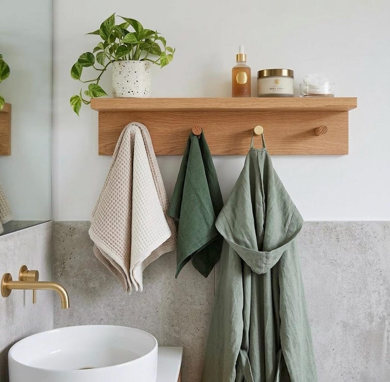 Bathroom towel holder in a modern bathroom with round sink and brass hardware. skin care on the shelf a trailing plant, and a robe hanging on a hook.