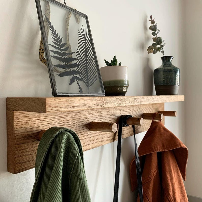 Solid Oak shaker style peg rail, with coats and a bag on the hooks, with decorative vase and leaves on top shelf.