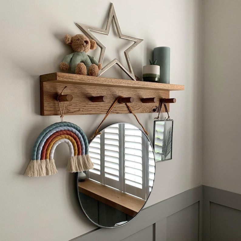 Oak shaker peg rail with 5 pegs and shelf on the top. with a mirror hanging of the pegs. nursery decor on the shelf.