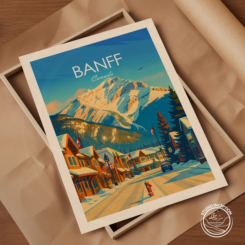 Puede incluir: Una impresi&oacute;n art&iacute;stica enmarcada que presenta una ilustraci&oacute;n estilizada de Banff, Canad&aacute;. La impresi&oacute;n representa una calle nevada con edificios, una cordillera y el texto "BANFF Canada" en blanco. La obra de arte est&aacute; sobre un cielo azul.