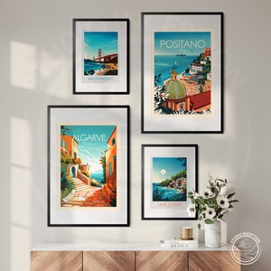 May include: Four framed travel posters with colorful illustrations of different cities. The posters are hung on a white wall. The posters feature the following cities: San Francisco, Positano, Algarve, and Lake Como.