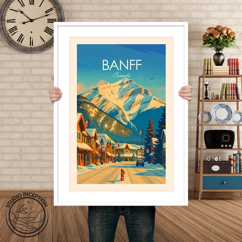 Puede incluir: Una impresi&oacute;n art&iacute;stica enmarcada de Banff, Canad&aacute;, que presenta una calle cubierta de nieve bordeada de edificios y una majestuosa cordillera en el fondo. La obra de arte tiene un estilo de cartel de viaje vintage con un cielo azul y la palabra "Banff" en la parte superior.