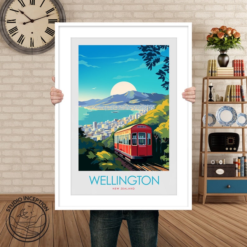 Może przedstawiać: Oprawiony wydruk artystyczny przedstawiający żywą ilustrację Wellington w Nowej Zelandii. Grafika przedstawia czerwoną kolejkę linową wspinającą się po bujnym, zielonym zboczu, z widokiem na miasto i port pod jasnym słońcem. Słowo "WELLINGTON" jest wydrukowane na niebiesko.