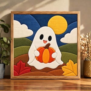 May include: A square framed fabric wall art piece featuring a white ghost holding an orange pumpkin. The scene includes a yellow sun, white clouds, green rolling hills, and brown ground with red and yellow maple leaves in a layered textile design.