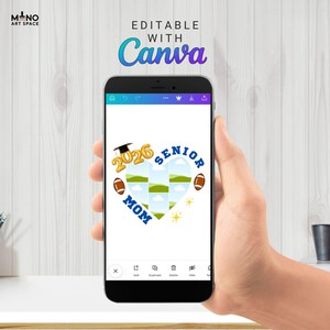 Pode incluir: Um smartphone exibe um design em forma de cora&ccedil;&atilde;o com o texto "2026 SENIOR MOM" e bolas de futebol americano. O design &eacute; edit&aacute;vel com Canva. O telefone &eacute; segurado em uma m&atilde;o contra um fundo claro de gr&atilde;o de madeira.