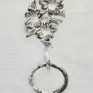 May include: Distressed white metal towel ring with a floral design. The top features three flowers and leaves. The ring is attached to the floral design by a small metal rod. The text "CozyRosefarm" and "74 Colors" are visible.