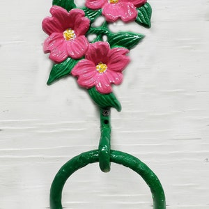May include: A decorative towel ring with a floral design. The metal ring is green, with three pink flowers and green leaves. The text "Berry Pink on Green" is at the bottom. The background is white.