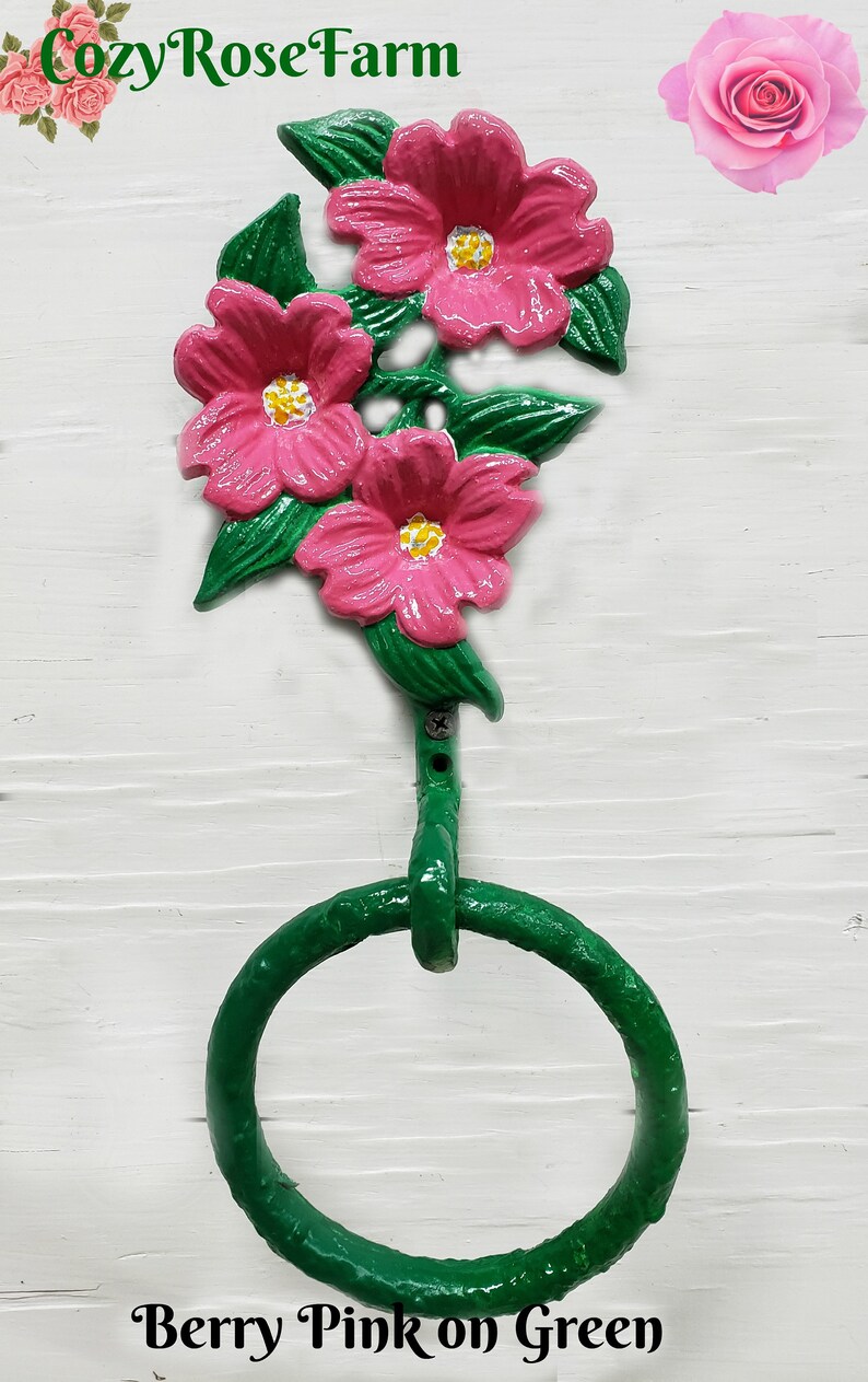 May include: A decorative towel ring with a floral design. The metal ring is green, with three pink flowers and green leaves. The text "Berry Pink on Green" is at the bottom. The background is white.