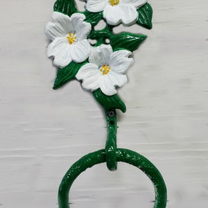 May include: A green dogwood flower towel ring with white flowers and yellow centers. The leaves are green, and the ring is also green. The text "Dogwood on meadow green" is at the bottom.