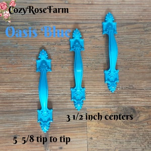 May include: Three Oasis Blue cabinet pulls with ornate detailing. The pulls are 5 5/8 inches tip to tip and 3 1/2 inch centers. The text "Cozy Rose Farm" and "Oasis Blue" are visible.