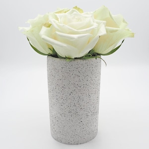 May include: A grey speckled vase with white roses. The vase is cylindrical with a textured surface. The roses are in full bloom, with soft, creamy petals. The vase is approximately 15 cm tall.