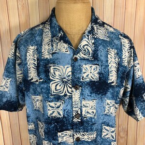 May include: A blue and white patterned short-sleeved button-up shirt with a relaxed fit. The shirt has a tropical print with a geometric design.