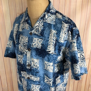 May include: A blue and white patterned short-sleeved button-up shirt with a relaxed fit. The shirt has a tropical print with white flowers and geometric designs on a blue background.