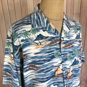 May include: A white short-sleeved button-down shirt with a blue and white tropical print. The print features palm trees, boats, and islands.