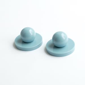 May include: Two light blue objects, each consisting of a smooth, spherical top piece attached to a flat, circular base. The items have a glossy, uniform finish and are positioned side by side, displaying a simple, geometric construction.