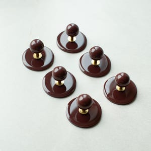 Rund knopp i mörkbrun/rödaktig/lila färg med bakplatta