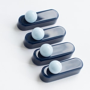Peut inclure: Quatre plateaux bleu marine et argentés, chacun contenant une sphère bleu clair. Les plateaux sont de forme rectangulaire avec des bords arrondis et un centre argenté. Les sphères sont lisses et uniformément colorées.