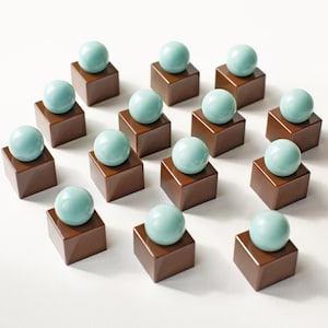 May include: A collection of fourteen individual pieces, each consisting of a smooth, glossy brown cube base topped with a single, solid light blue sphere. The items are arranged in a grid-like formation on a plain white surface.