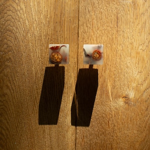 Op de afbeelding: Twee vierkante kastknoppen met ingebedde gedroogde vruchten en hars. De knoppen zijn gemonteerd op een houten kastdeur. Het fruit is zichtbaar door de heldere hars. De knoppen werpen lange schaduwen op het hout.