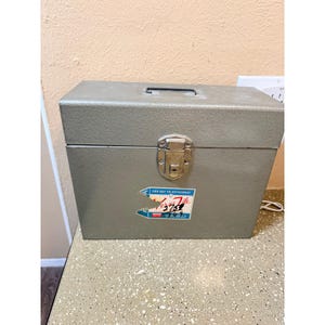 May include: A grey metal toolbox with a handle and latch. A sticker on the front reads "For Key to Efficiency" and "Versa-File 3752". The box is rectangular and appears to be vintage.