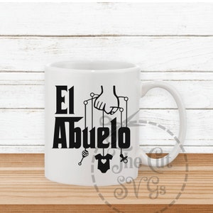 May include: White ceramic mug with a black design that says "El Abuelo" with a hand holding strings attached to a baby rattle, a baby onesie, and a pacifier.