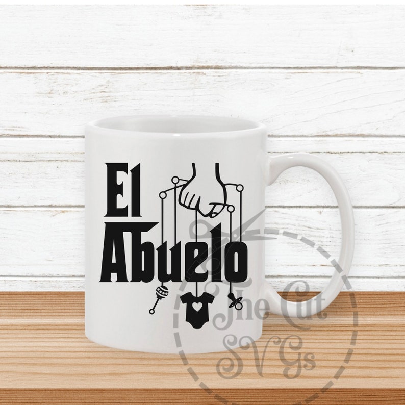 May include: White ceramic mug with a black design that says "El Abuelo" with a hand holding strings attached to a baby rattle, a baby onesie, and a pacifier.